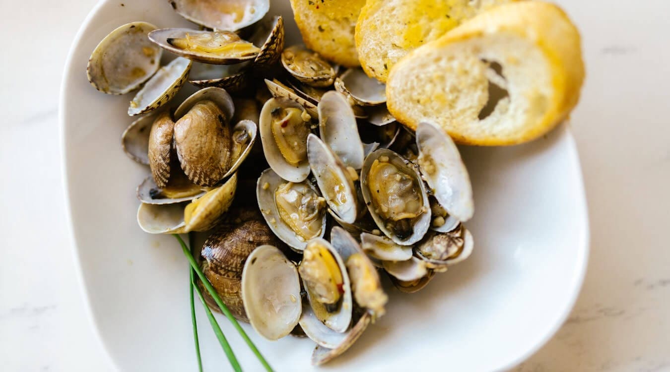 Cooked Clams in half shell in a bowl with bread.