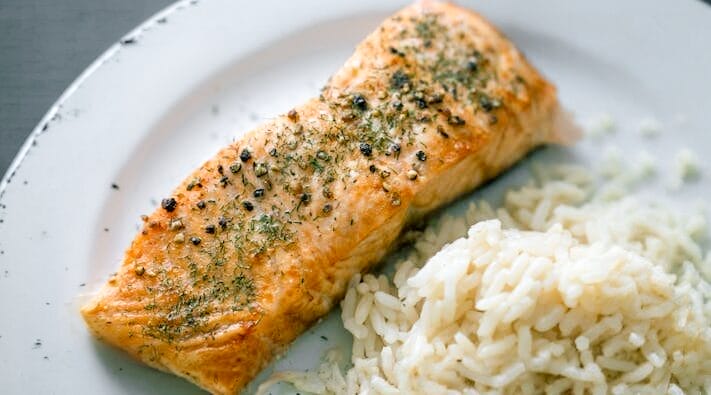 A piece of fish plated with a side of white rice.