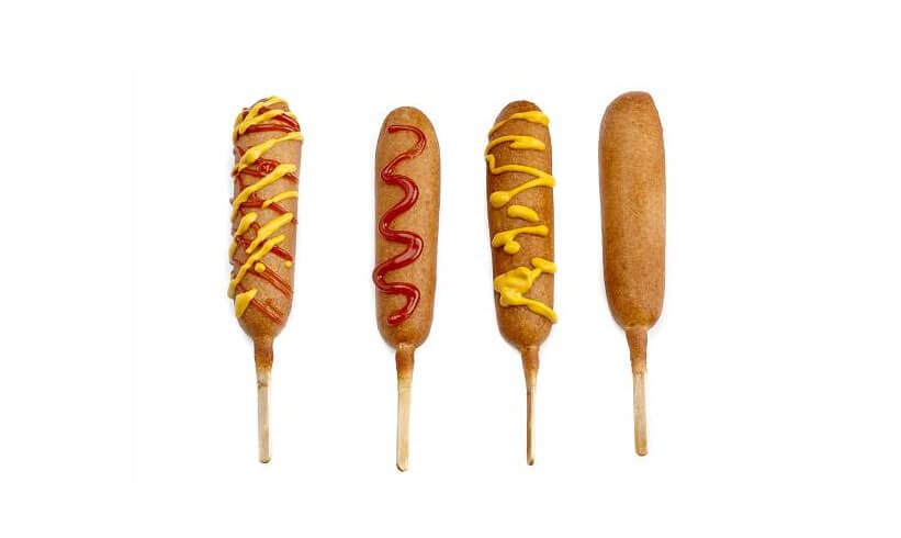 Corn dogs on a stick with ketchup and mustard.