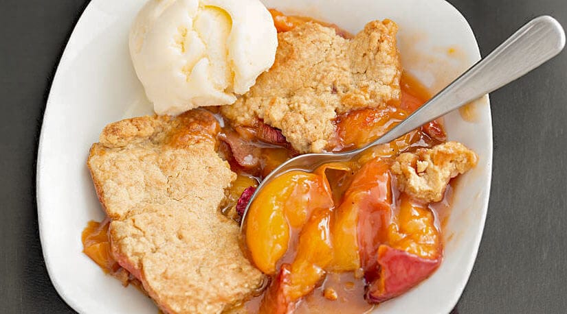 Bowl of peach cobbler with a scoop of ice cream.